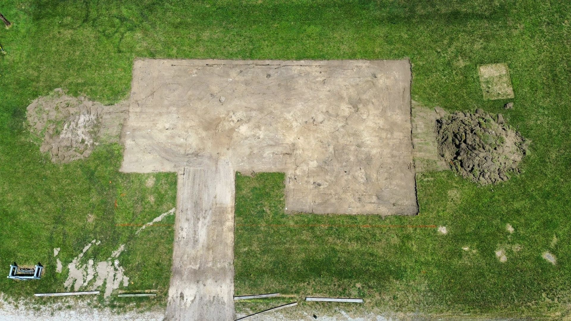 An aerial view of an archaeological excavation site featuring rectangular cleared earth patches surrounded by green grass.
