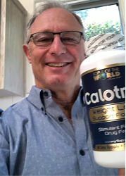 Man holding a supplement bottle, smiling. Bottle label reads "Calotren". Blue shirt, glasses, interior setting.