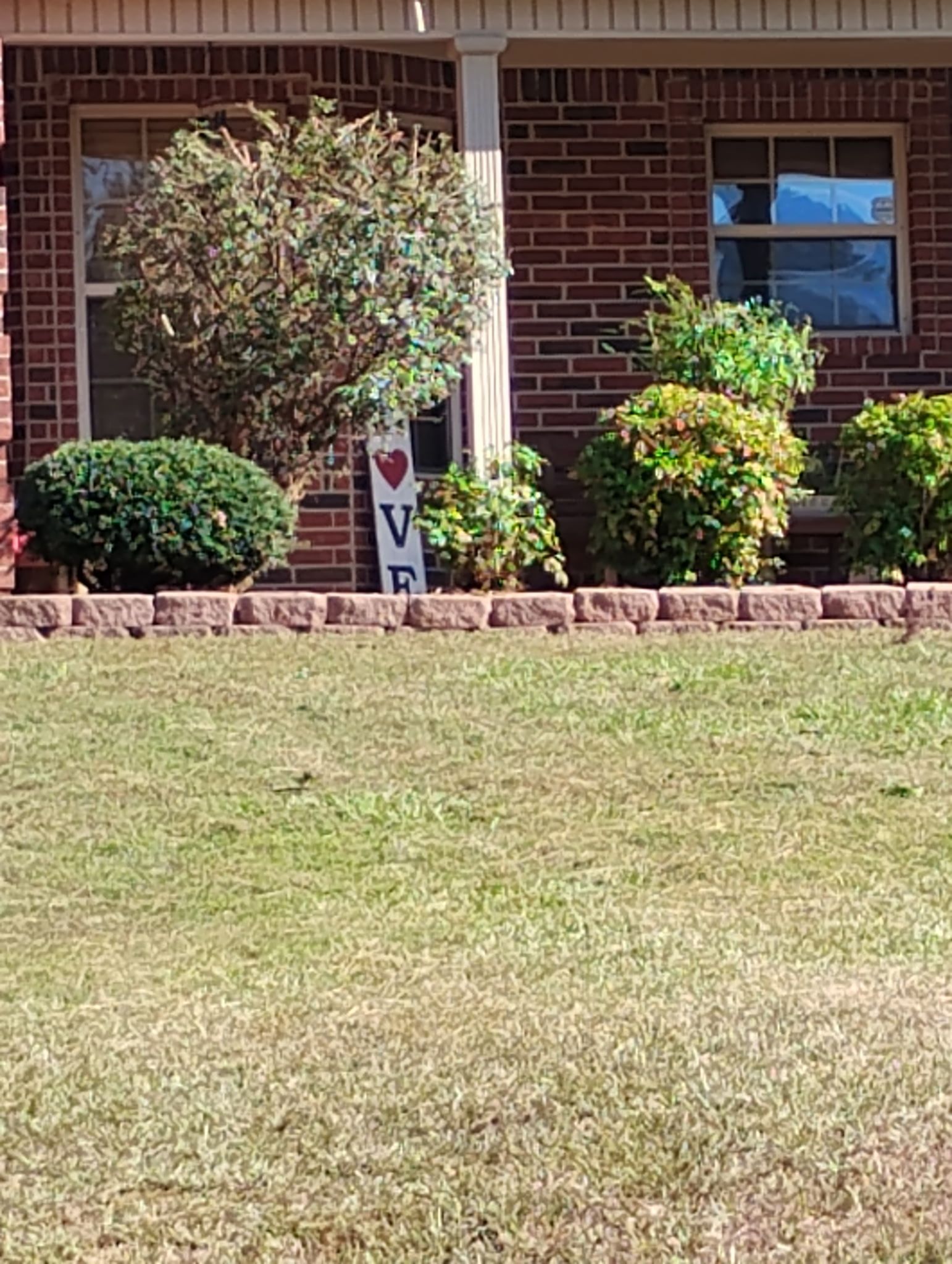 A brick house in front of bushes and a lawn