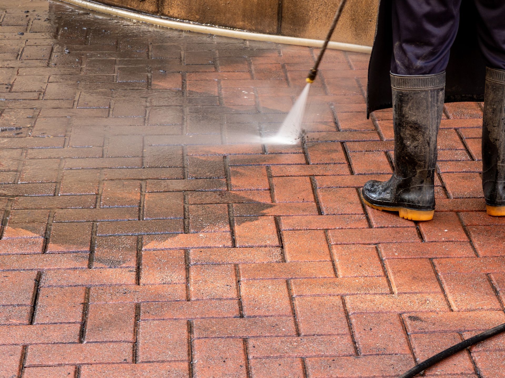 Person power washing a brick patio, cleaning the surface with a jet of water