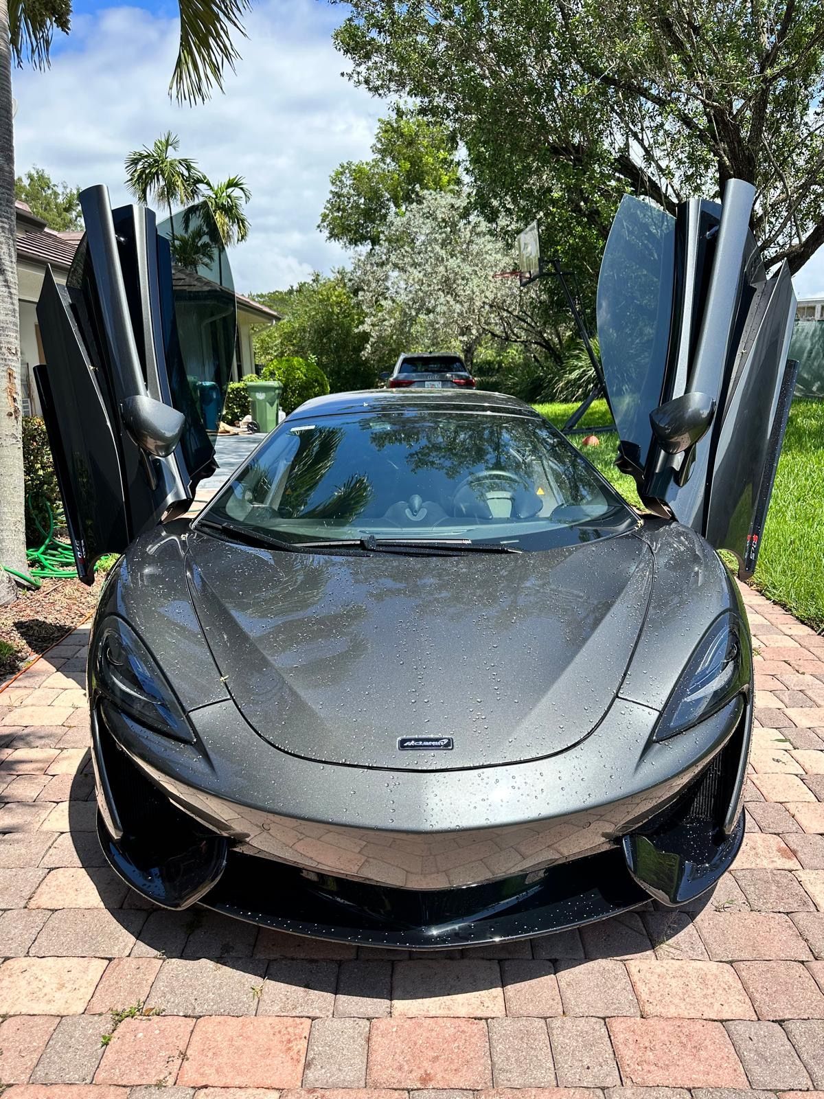 A gray sports car is parked on a brick driveway with its doors open.