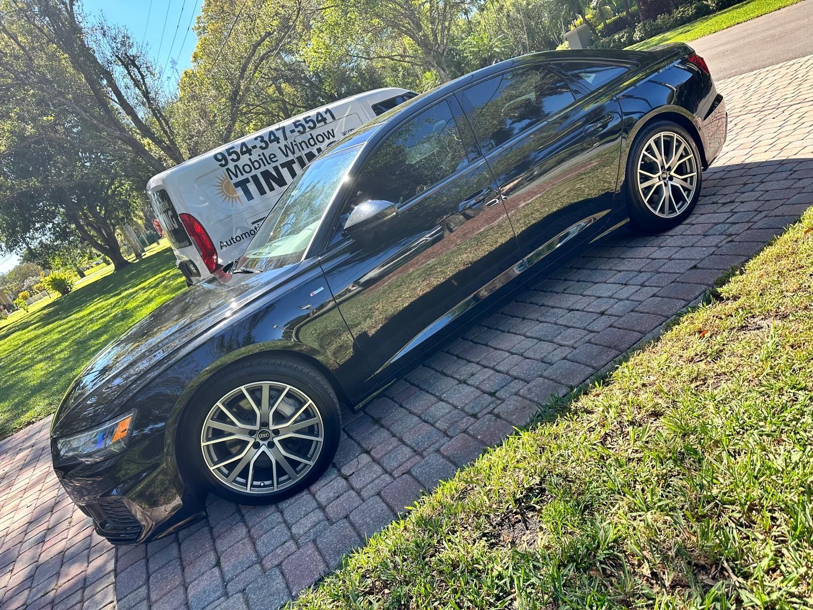 A black car is parked on a brick driveway next to a white van.