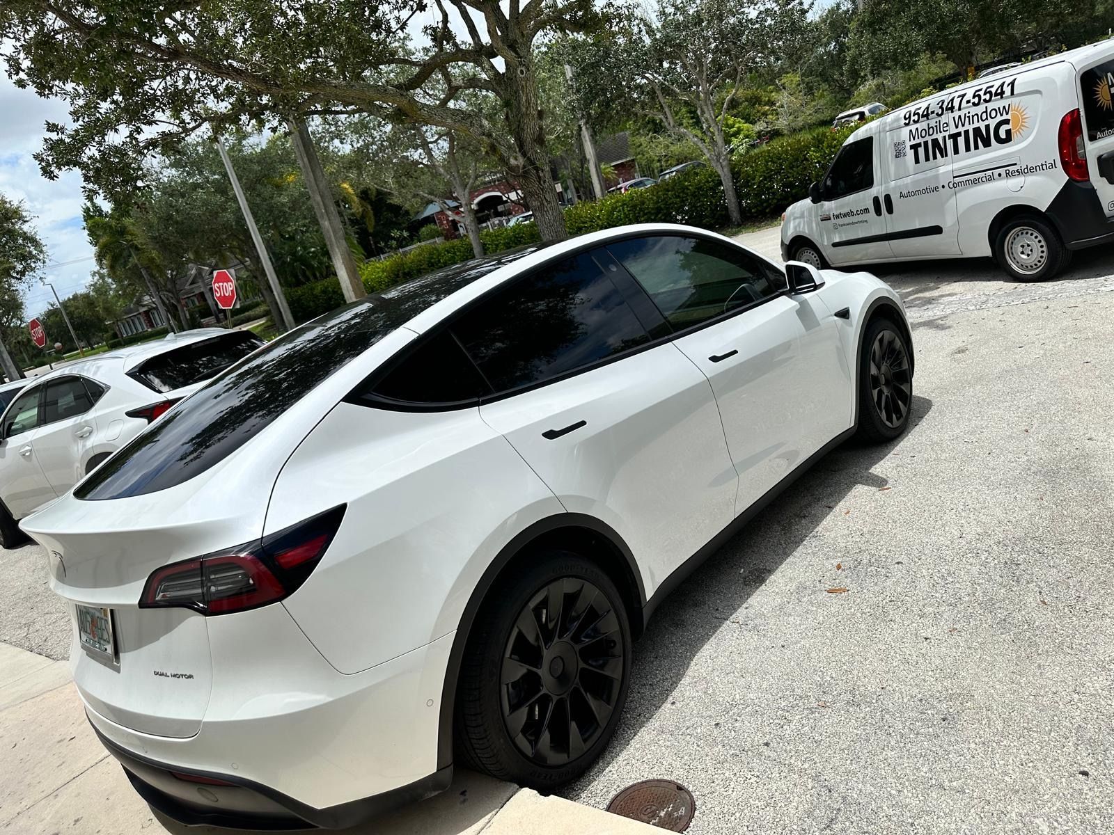 A white tesla model y is parked in a parking lot next to a van.
