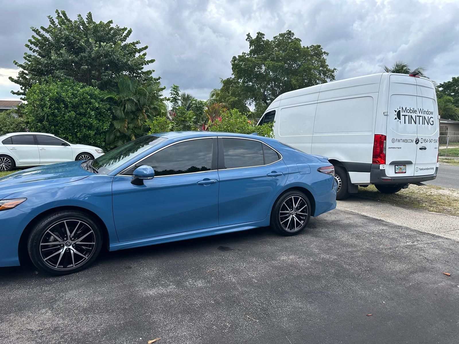 A blue car is parked next to a white van in a driveway.