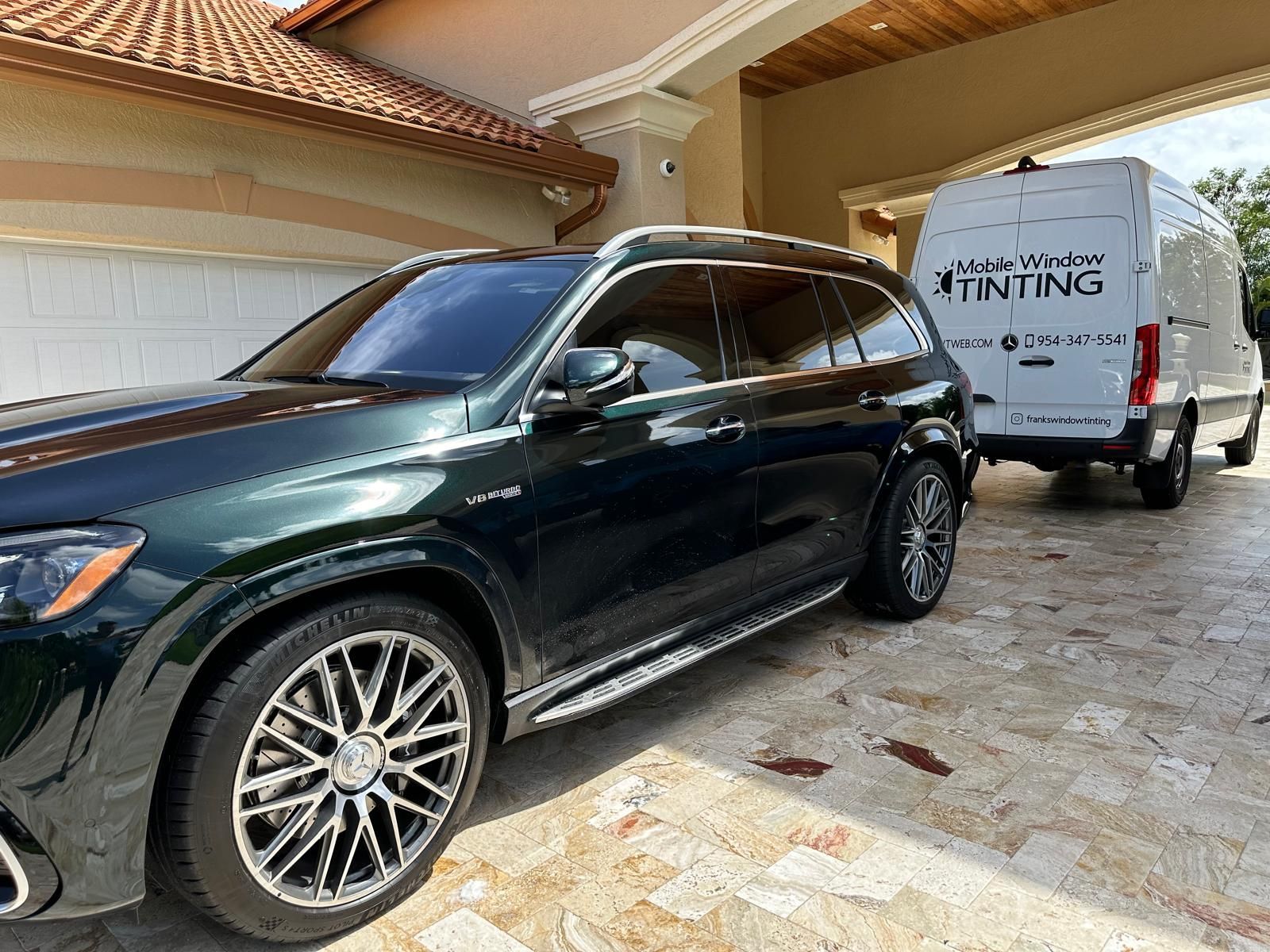 A black suv is parked in front of a house next to a white van.