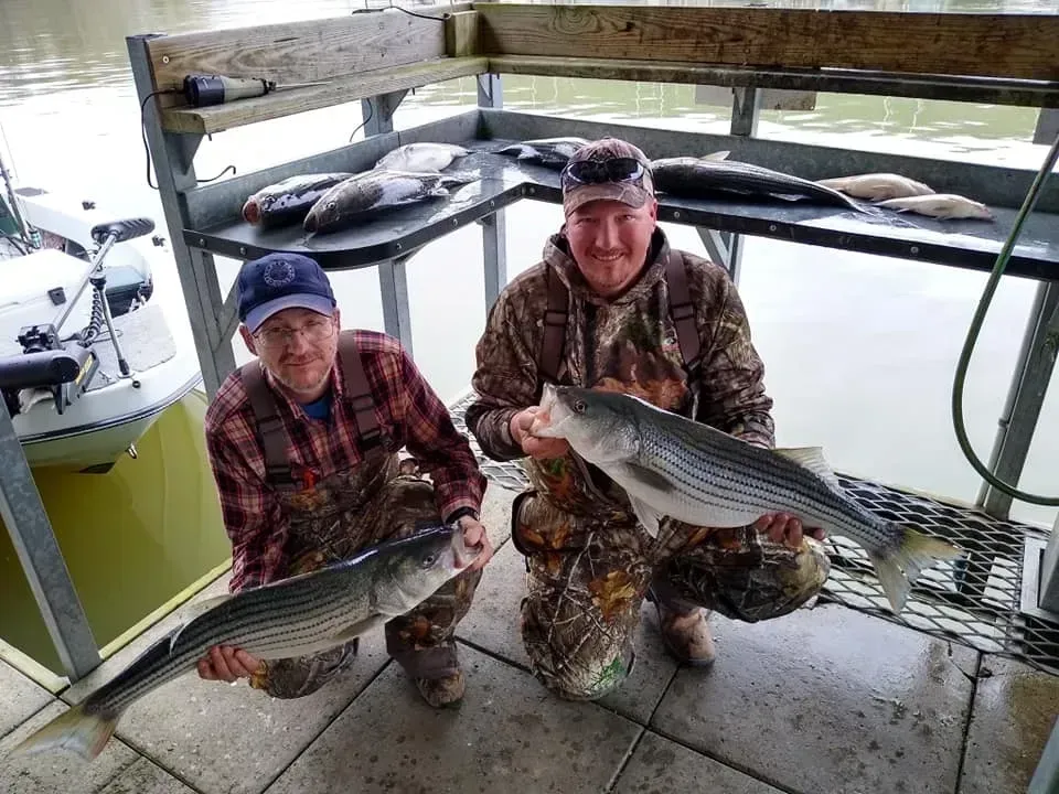 Two people hold up striped fish they caught near a cleaning station, with other fish visible.