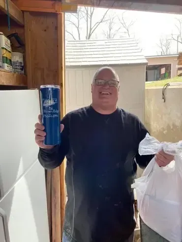 Man holding a blue tumbler and a bag, smiling in a doorway.