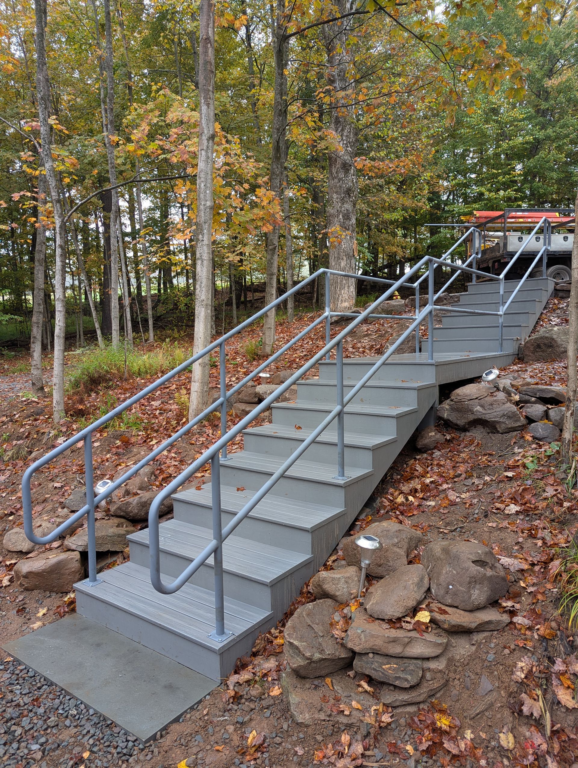 Gray metal staircase with handrails in a wooded area, leading uphill.