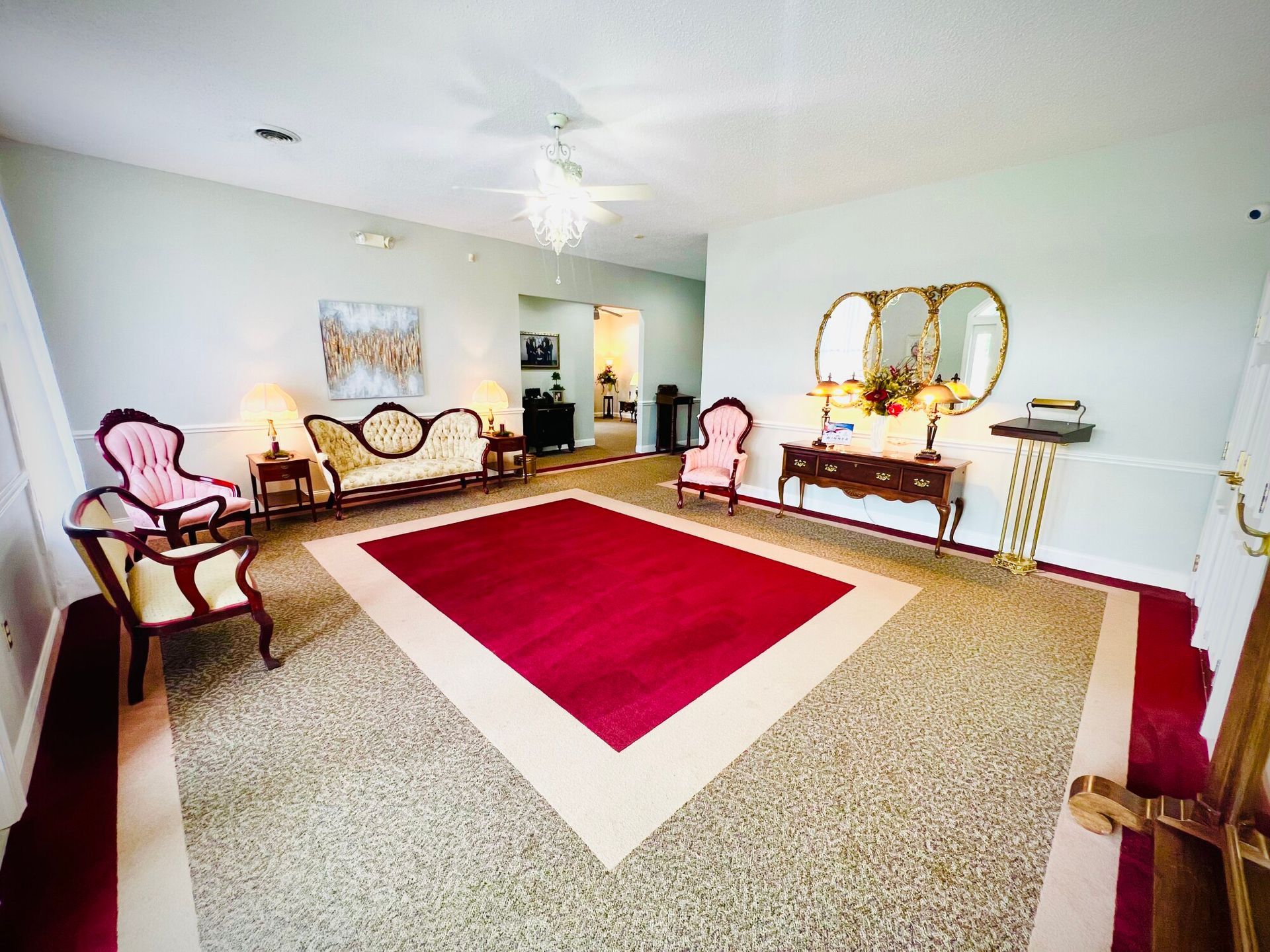 Formal reception area with antique furniture, red carpet, and ornate gold mirror.
