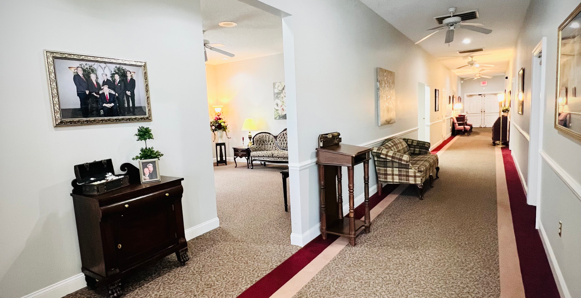 Hallway with chairs, artwork, and dark wooden furniture. Beige carpet with red runner.