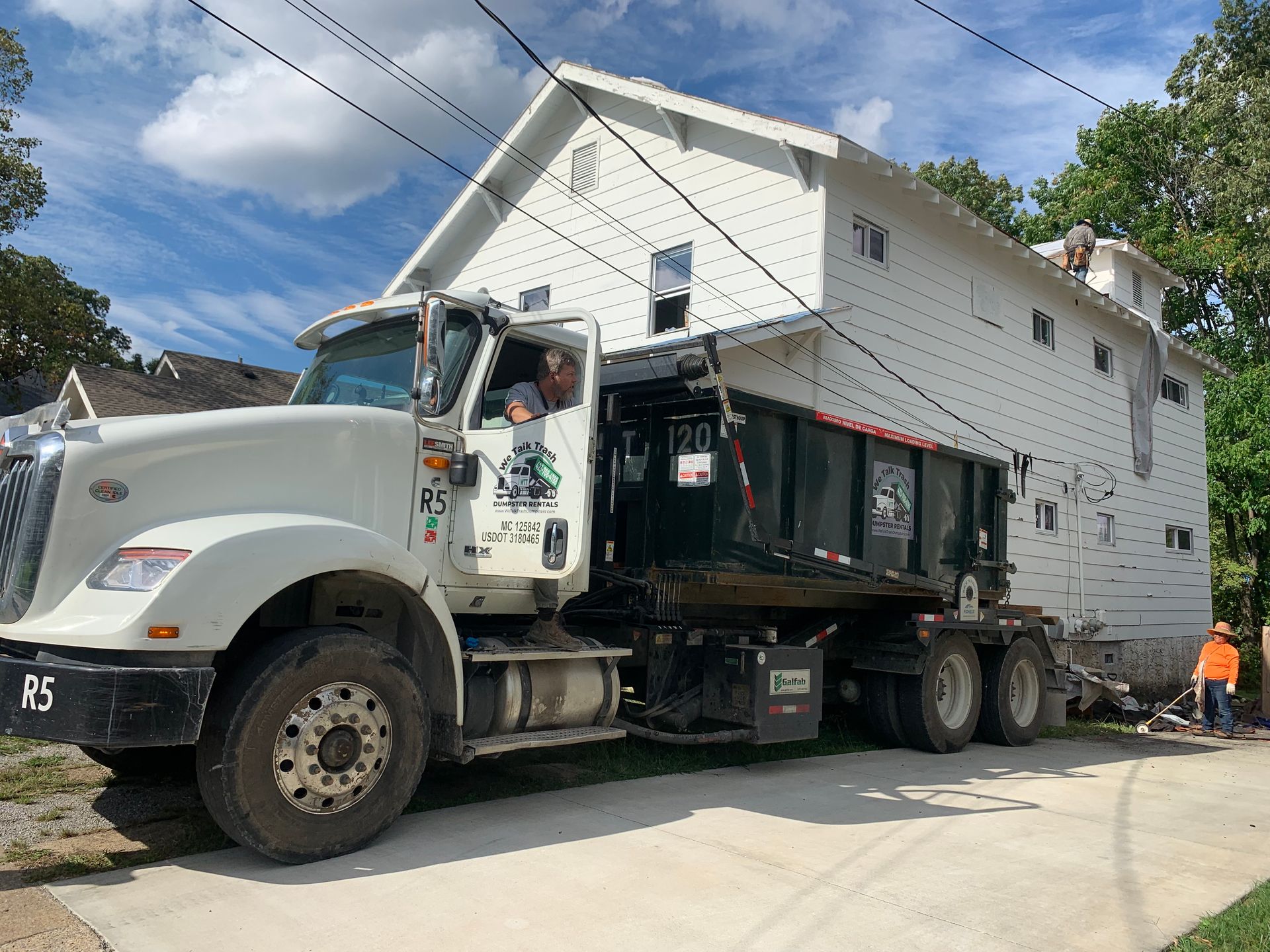 A dump truck is parked in front of a white house.