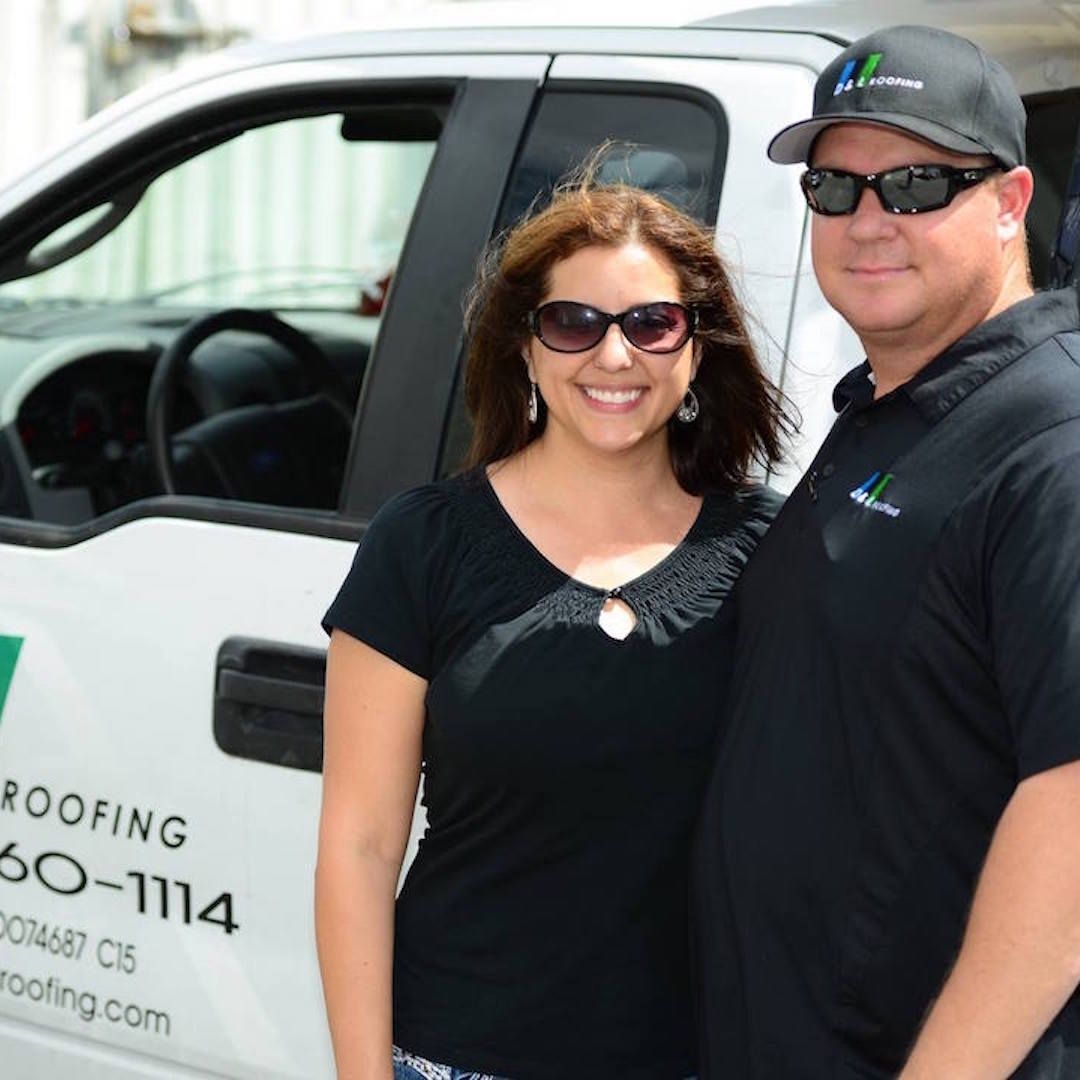 A man and a woman standing in front of a roofing truck