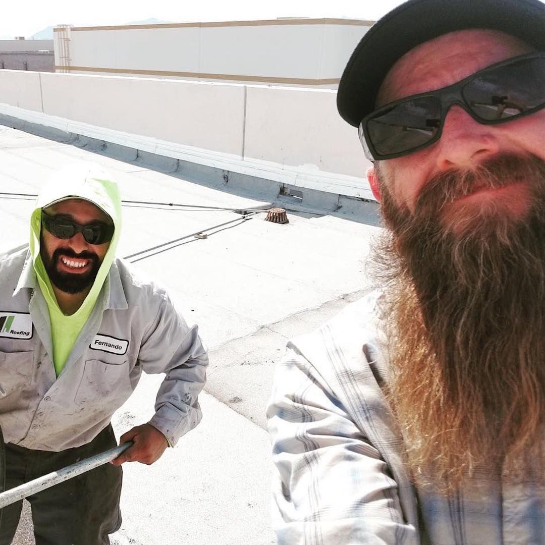A man with a beard is standing next to another man wearing sunglasses