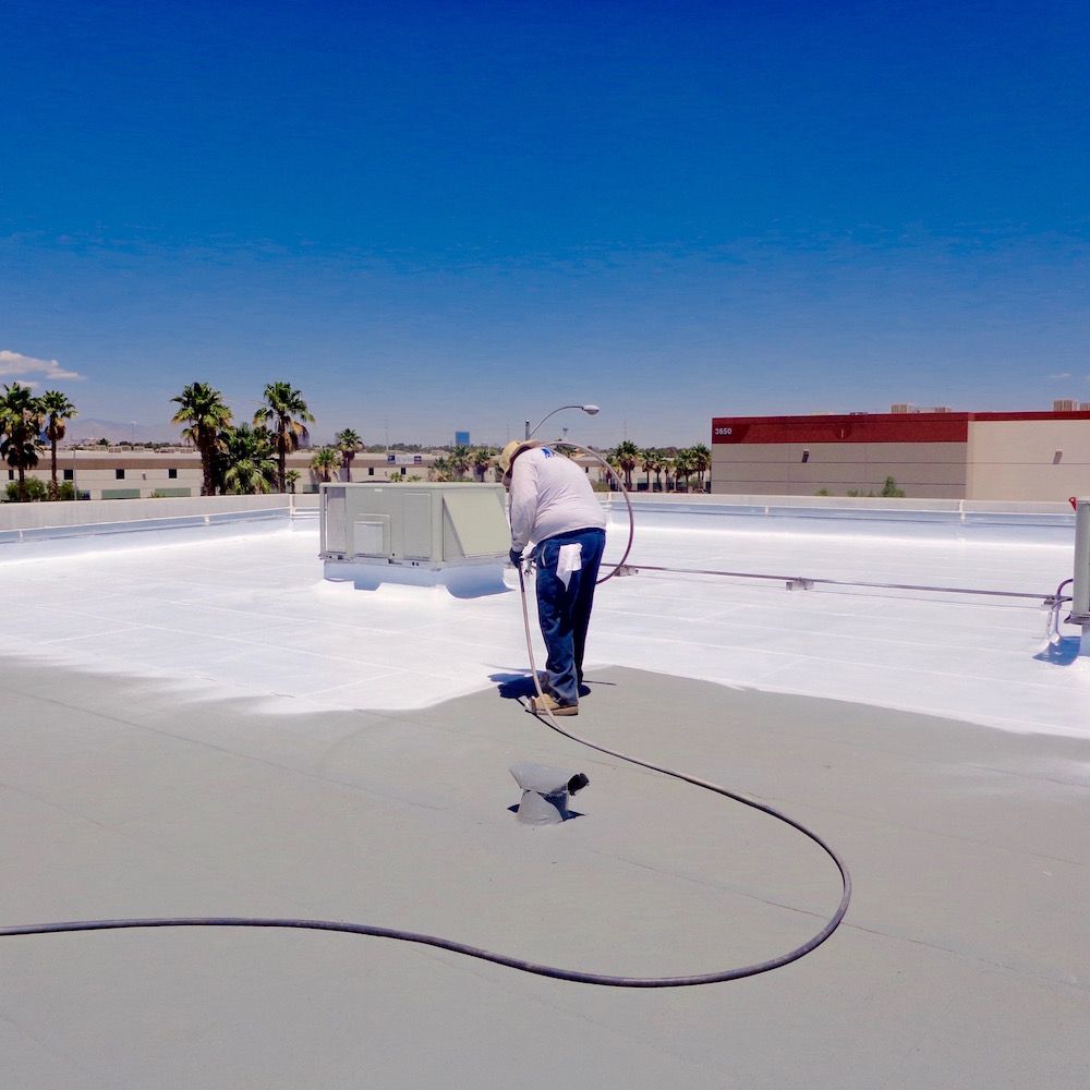 A man is spraying a roof with a white coating