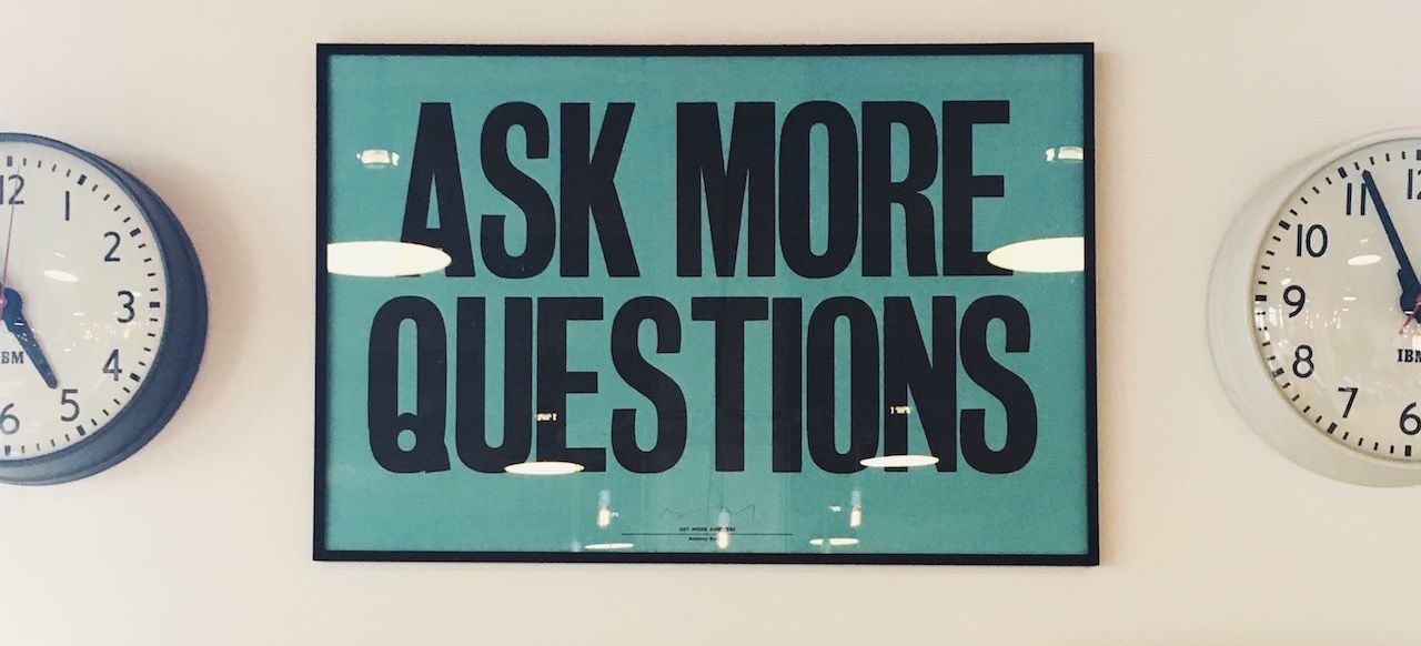 A sign on a wall that says ask more questions
