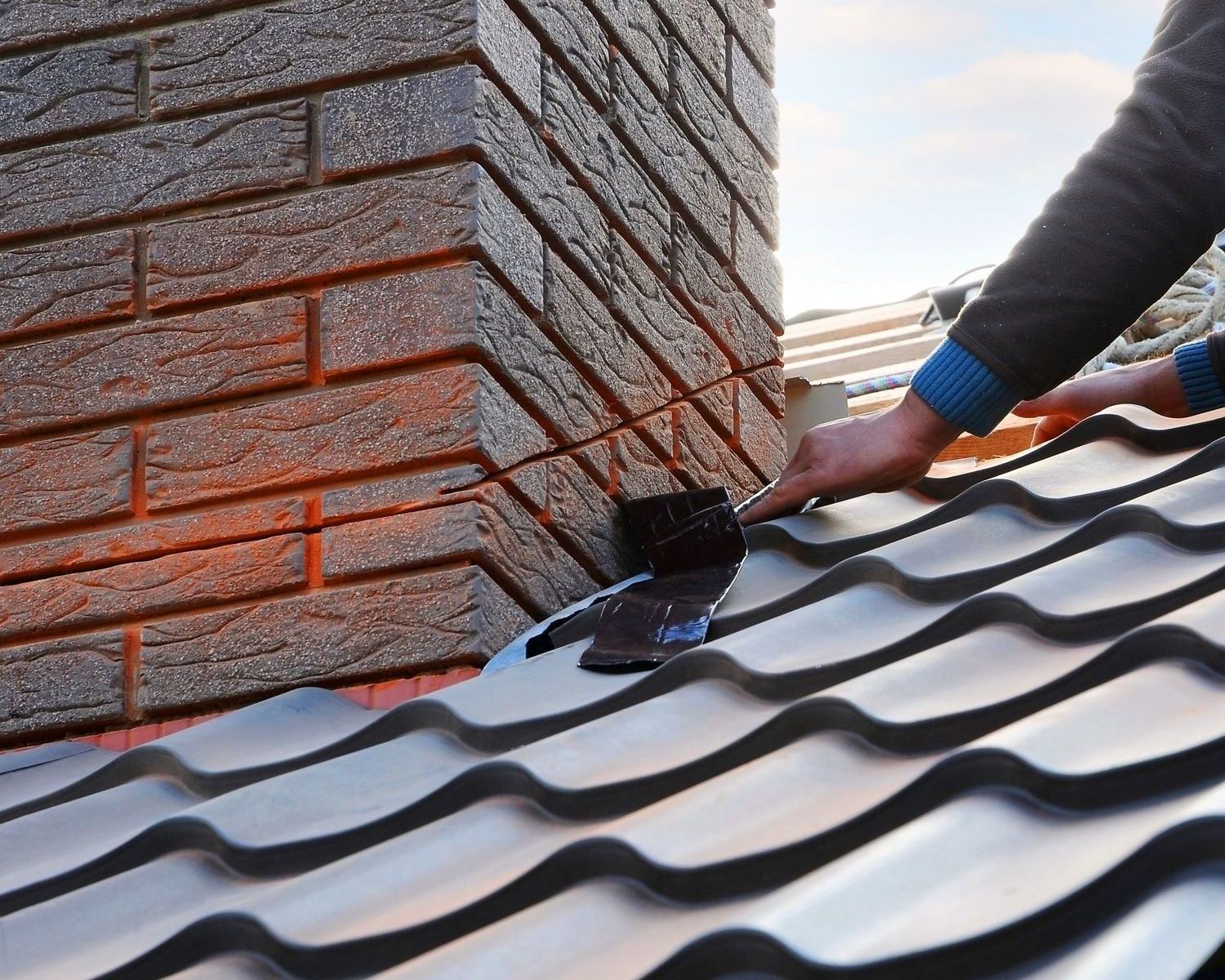 A person is working on a roof with a brick chimney in the background.