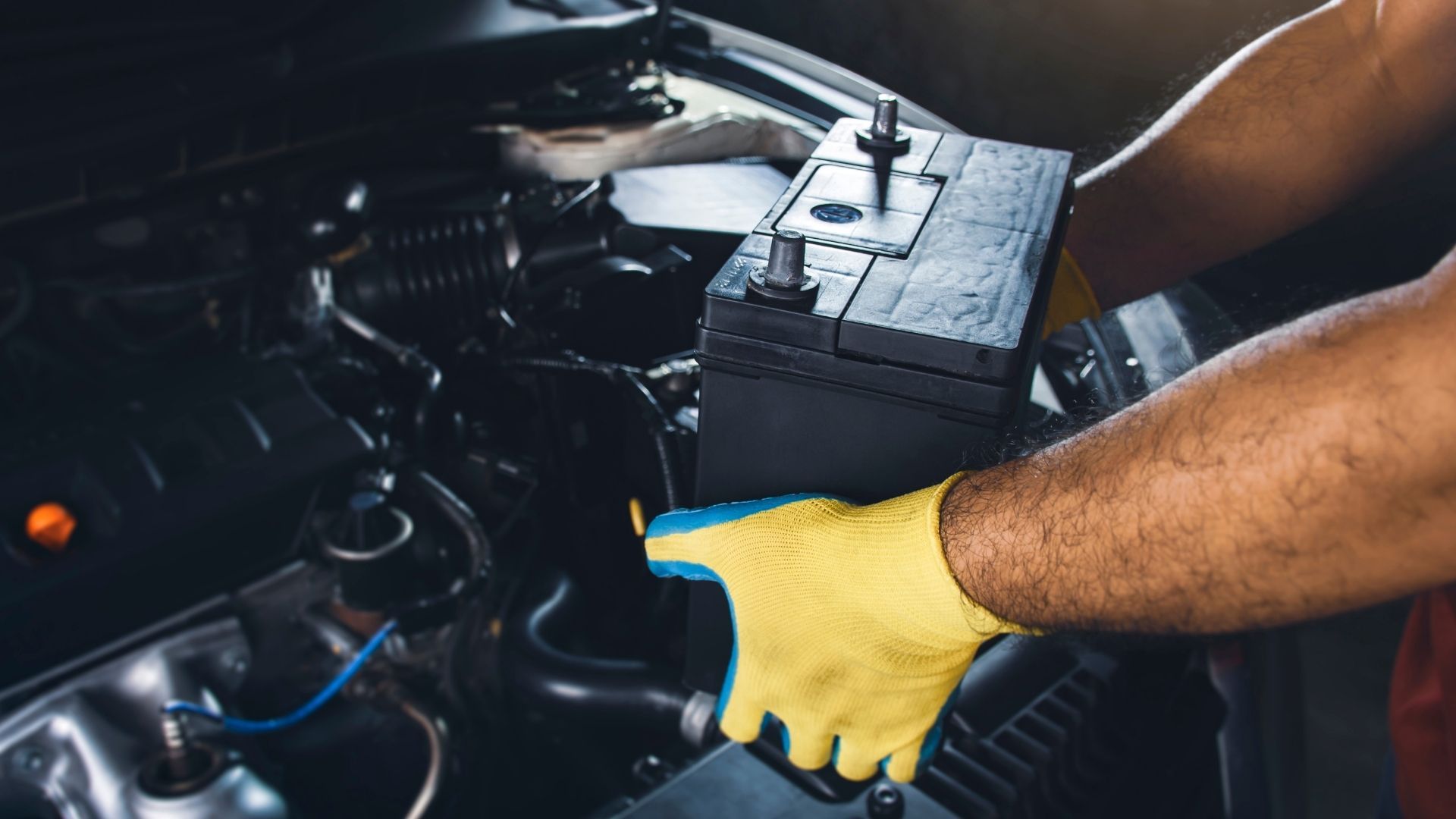 A man wearing yellow gloves is working on a car battery.
