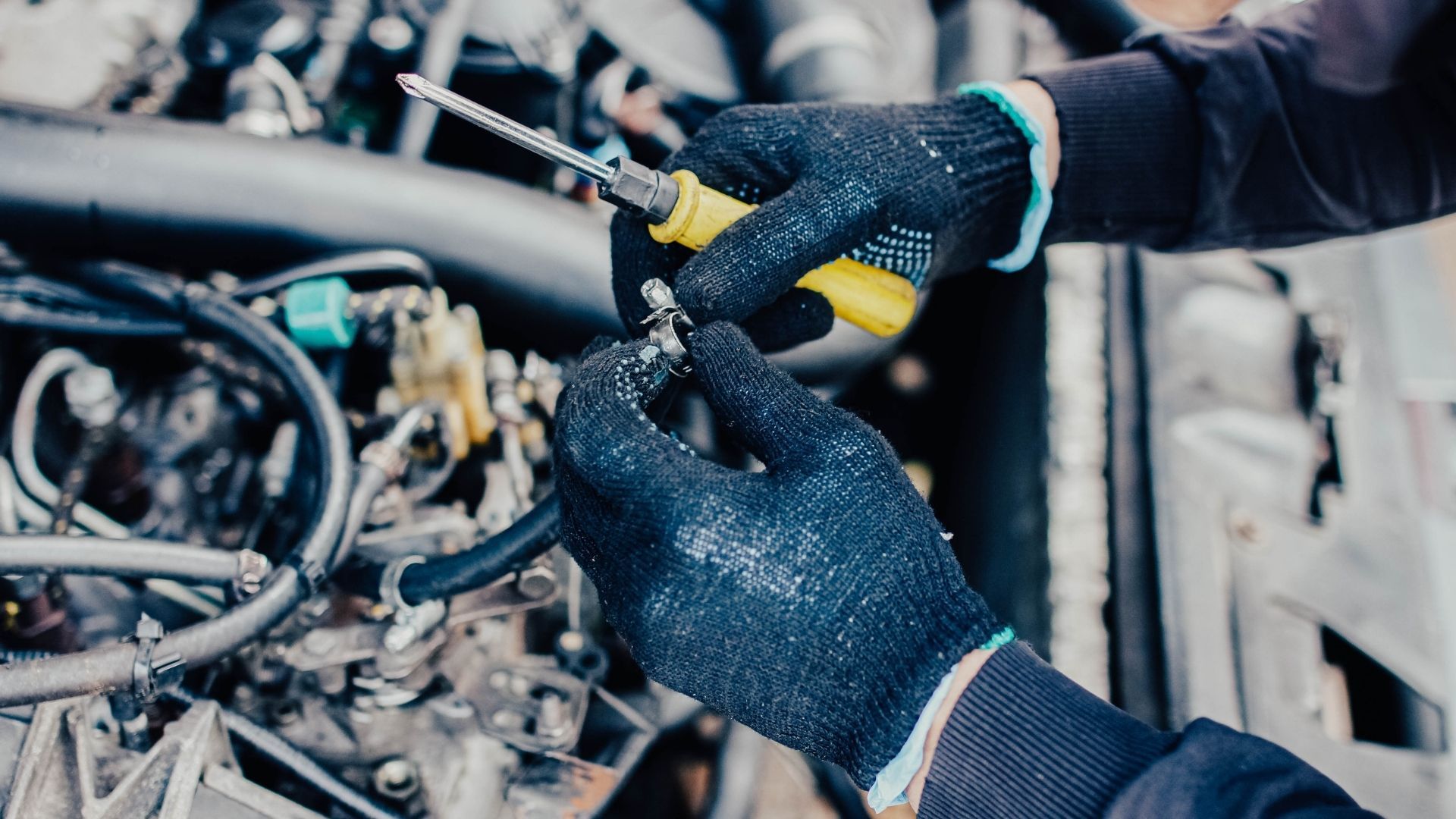 A person is working on a car engine with a screwdriver.