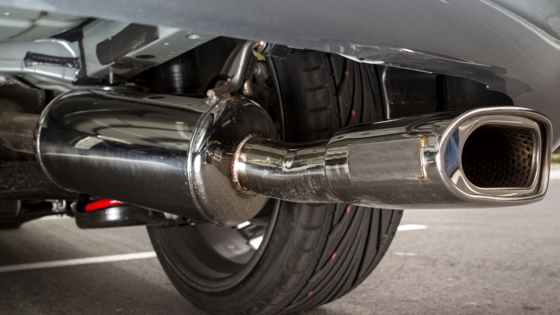 A car with a stainless steel exhaust pipe is parked in a parking lot.