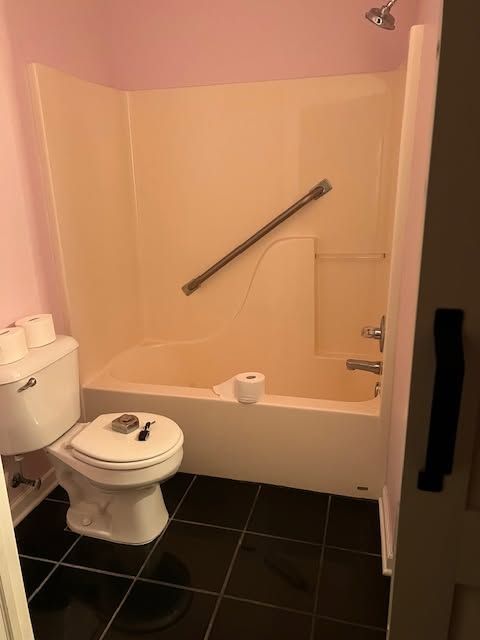 Accessible bathroom with tub-shower, grab bar, toilet, and black tile floor