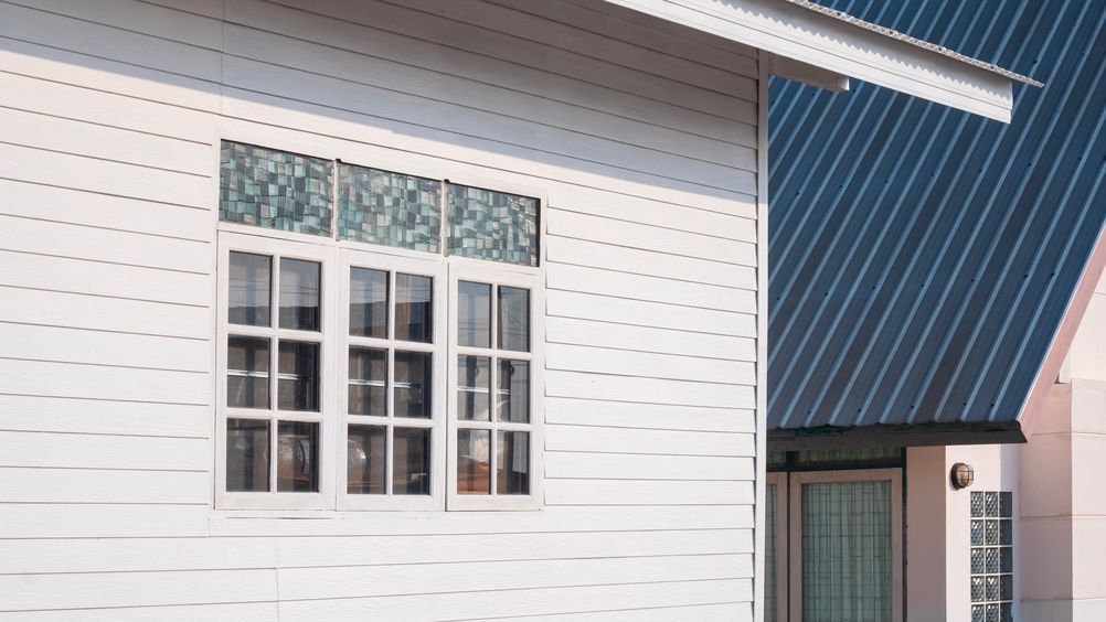 White house exterior with a window, decorative trim, and a blue metal roof section