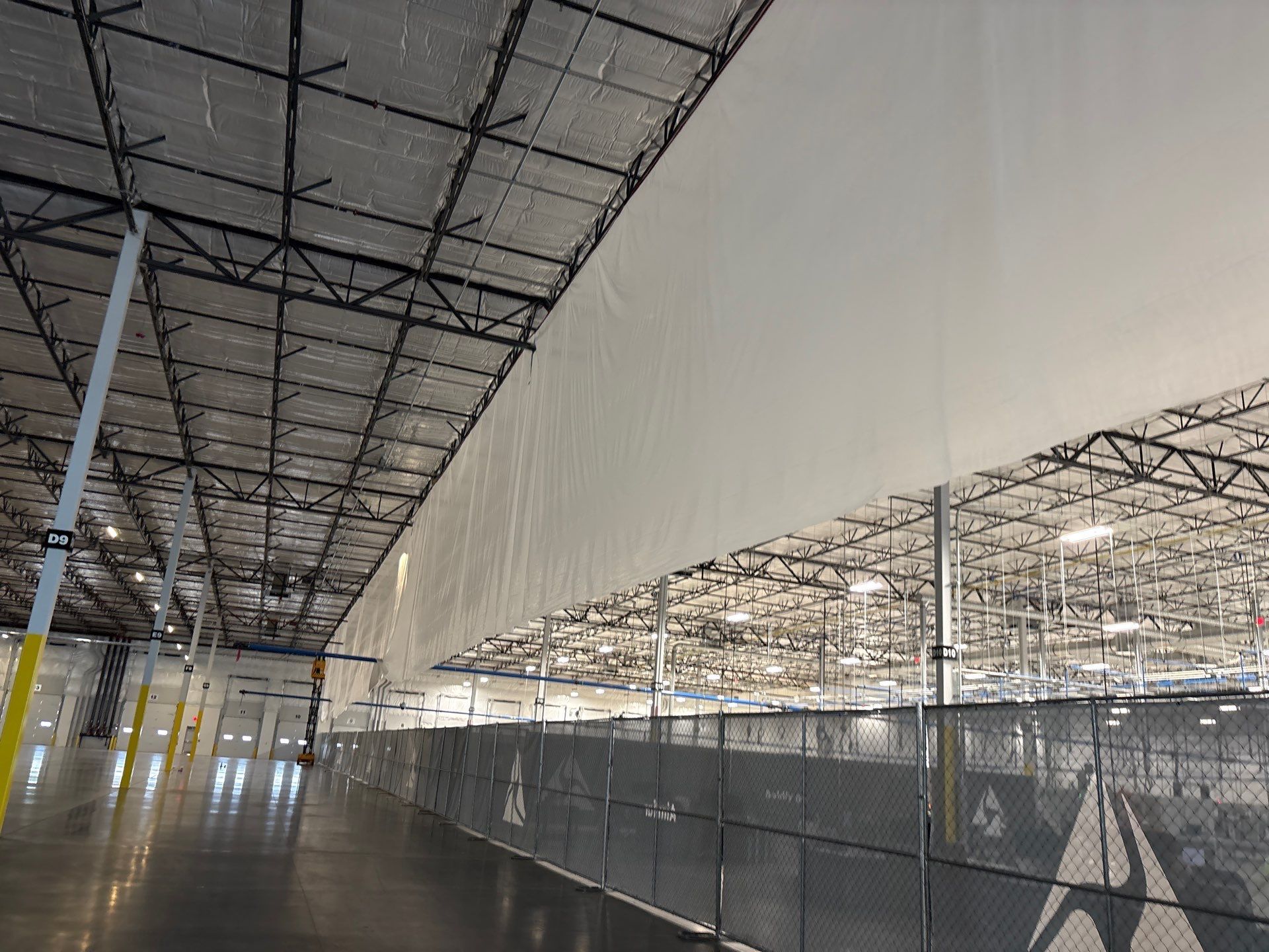 Empty industrial warehouse with scaffolding, mesh fencing, and a large white wall panel under construction