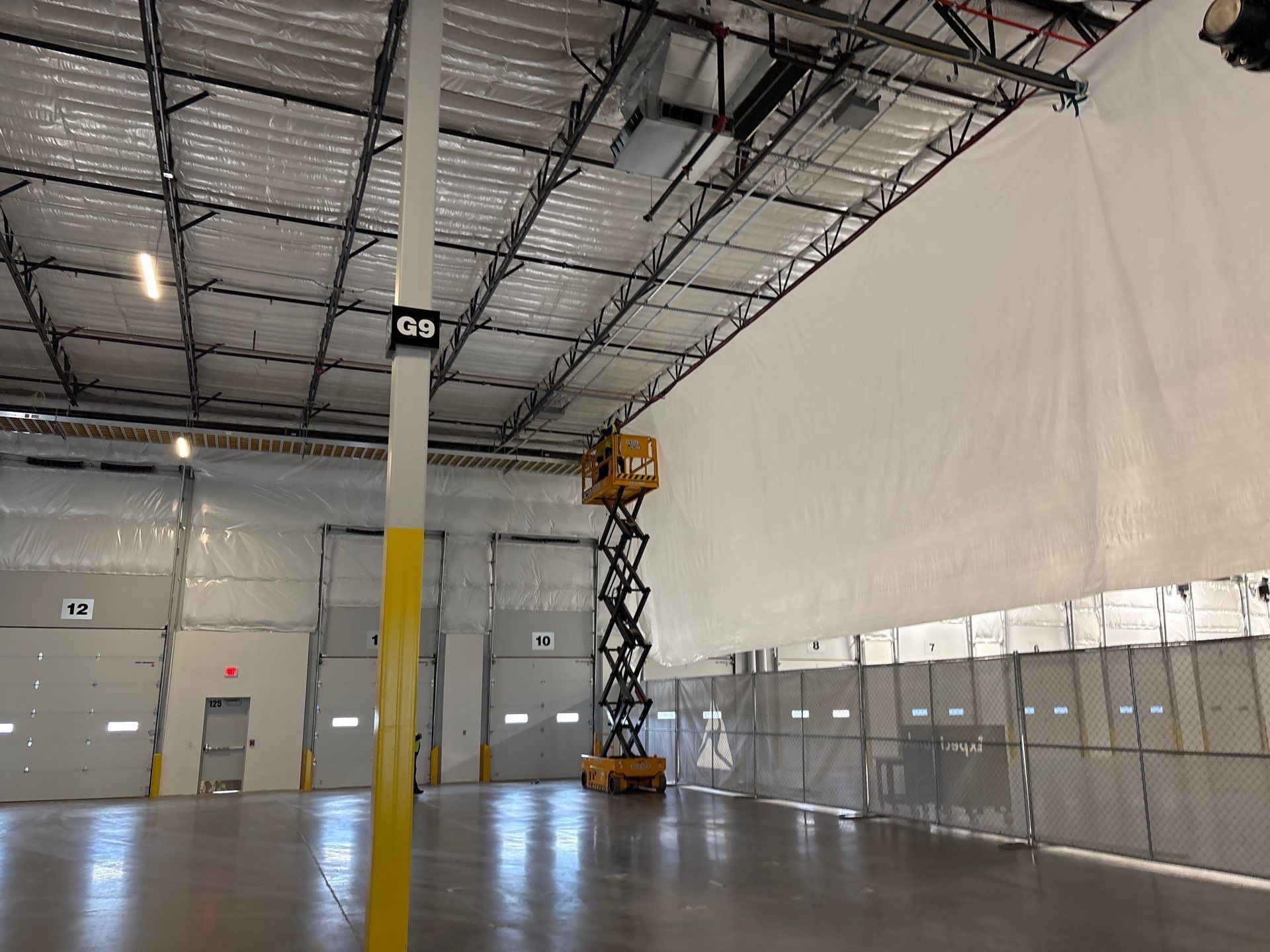Empty warehouse interior with a scissor lift near a tall white wall and metal doors