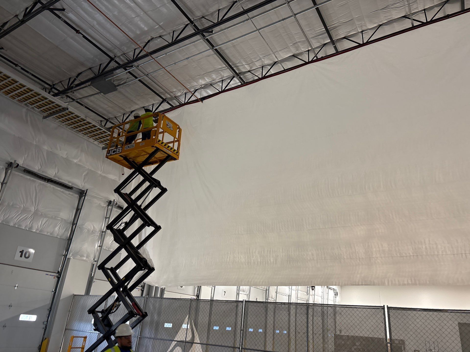 Scissor lift raised beside a large white wall inside a warehouse-like room
