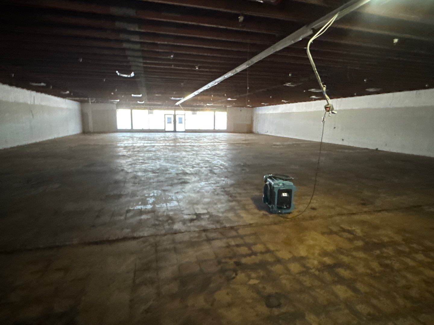 Empty industrial warehouse with a concrete floor, exposed beams, and a small generator near the front.