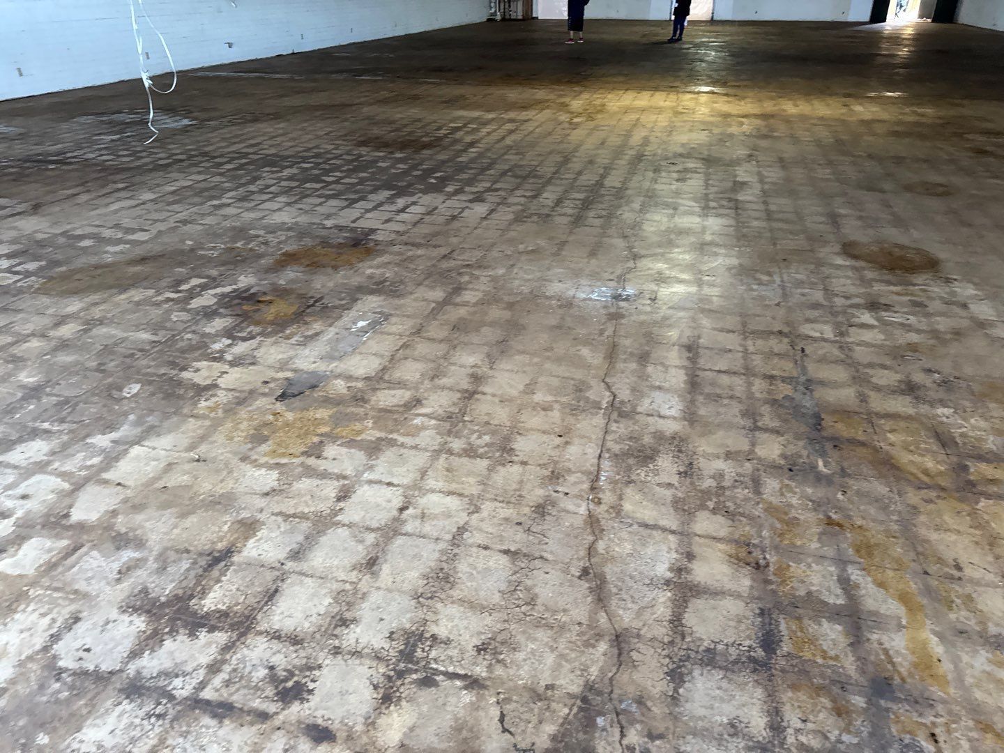 Empty indoor room with worn brown tiled floor and white walls, viewed from a low angle