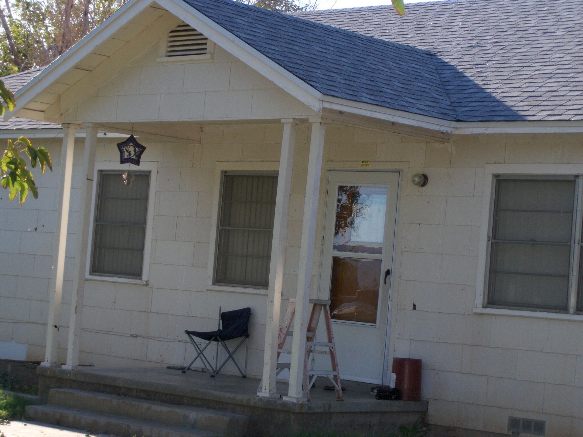 Small white house porch with ladder, chair, and hanging lantern under a blue roof.