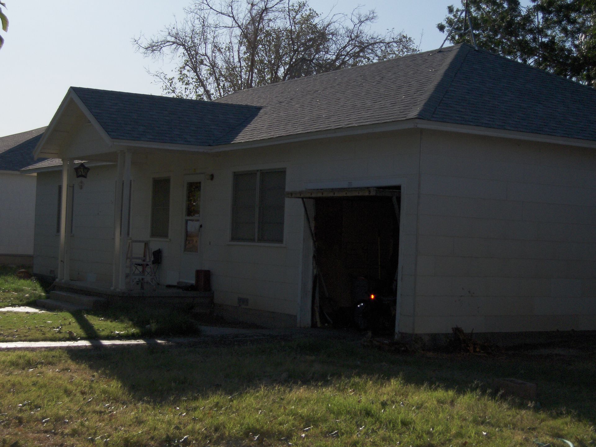 Single-story beige house with a dark roof and open garage door in daylight.