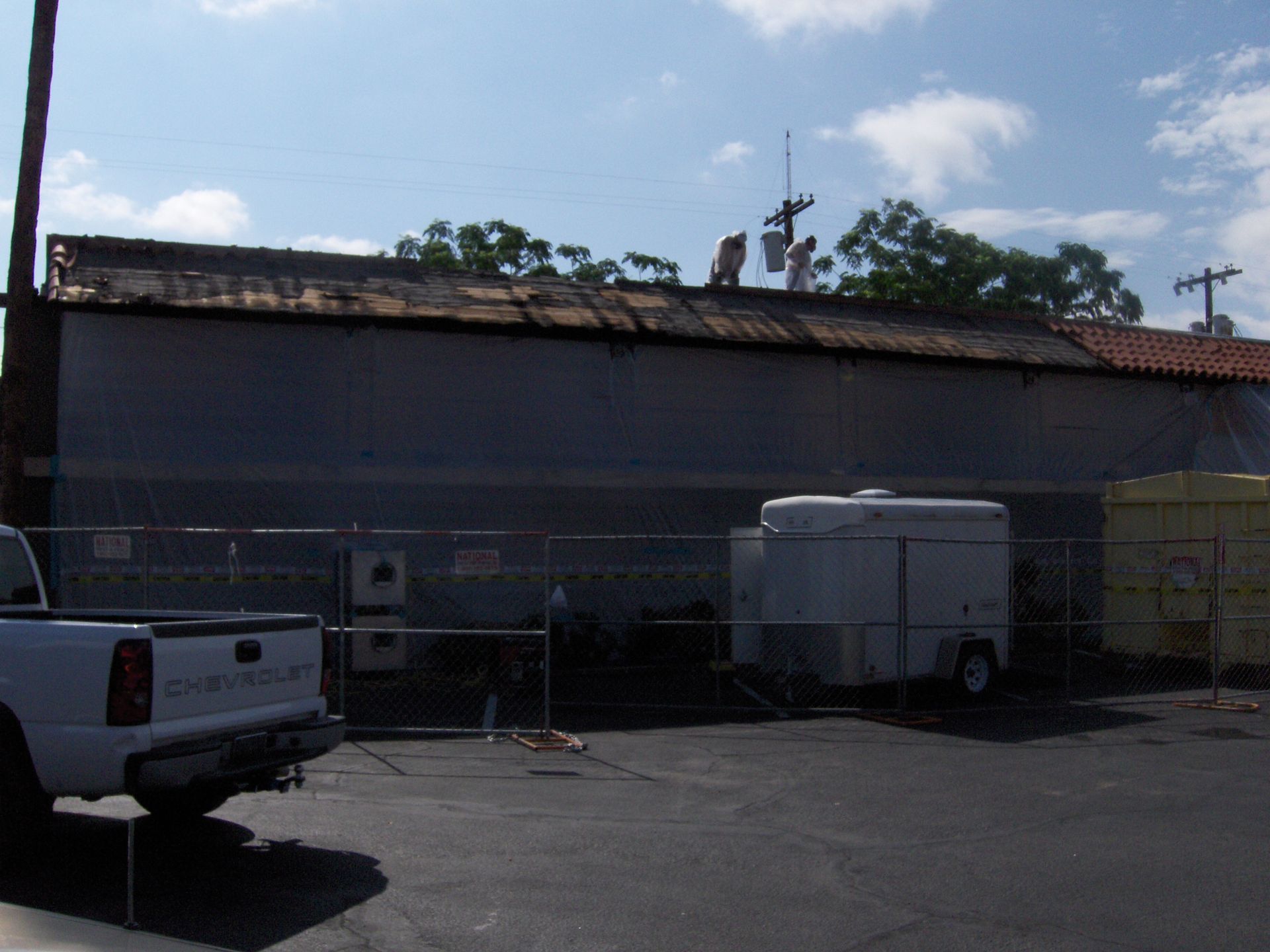 Parking lot beside a building with a white pickup truck and a small trailer under a cloudy sky