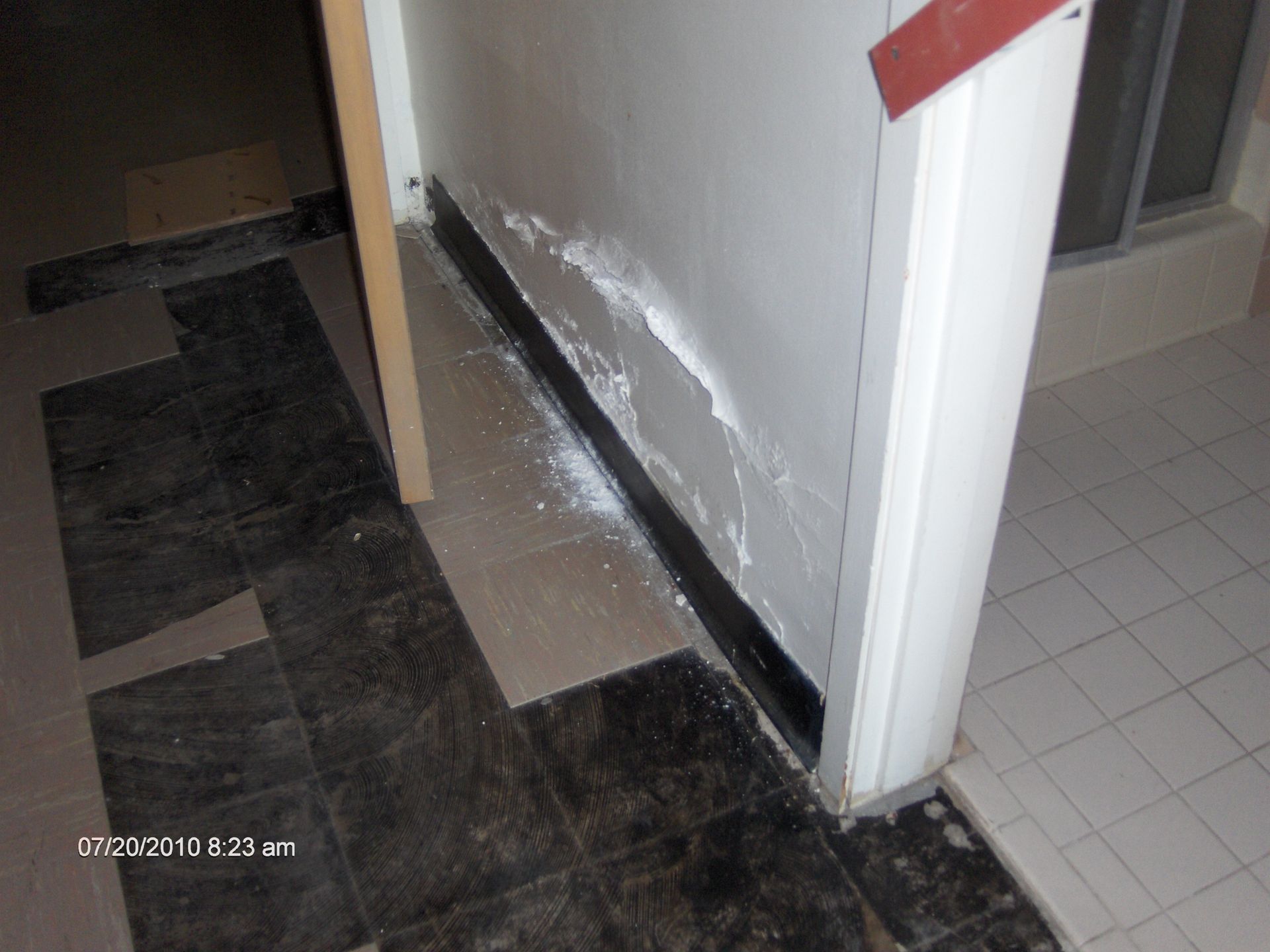 Hallway floor with loose black tiles and damaged white wall paint near a doorway
