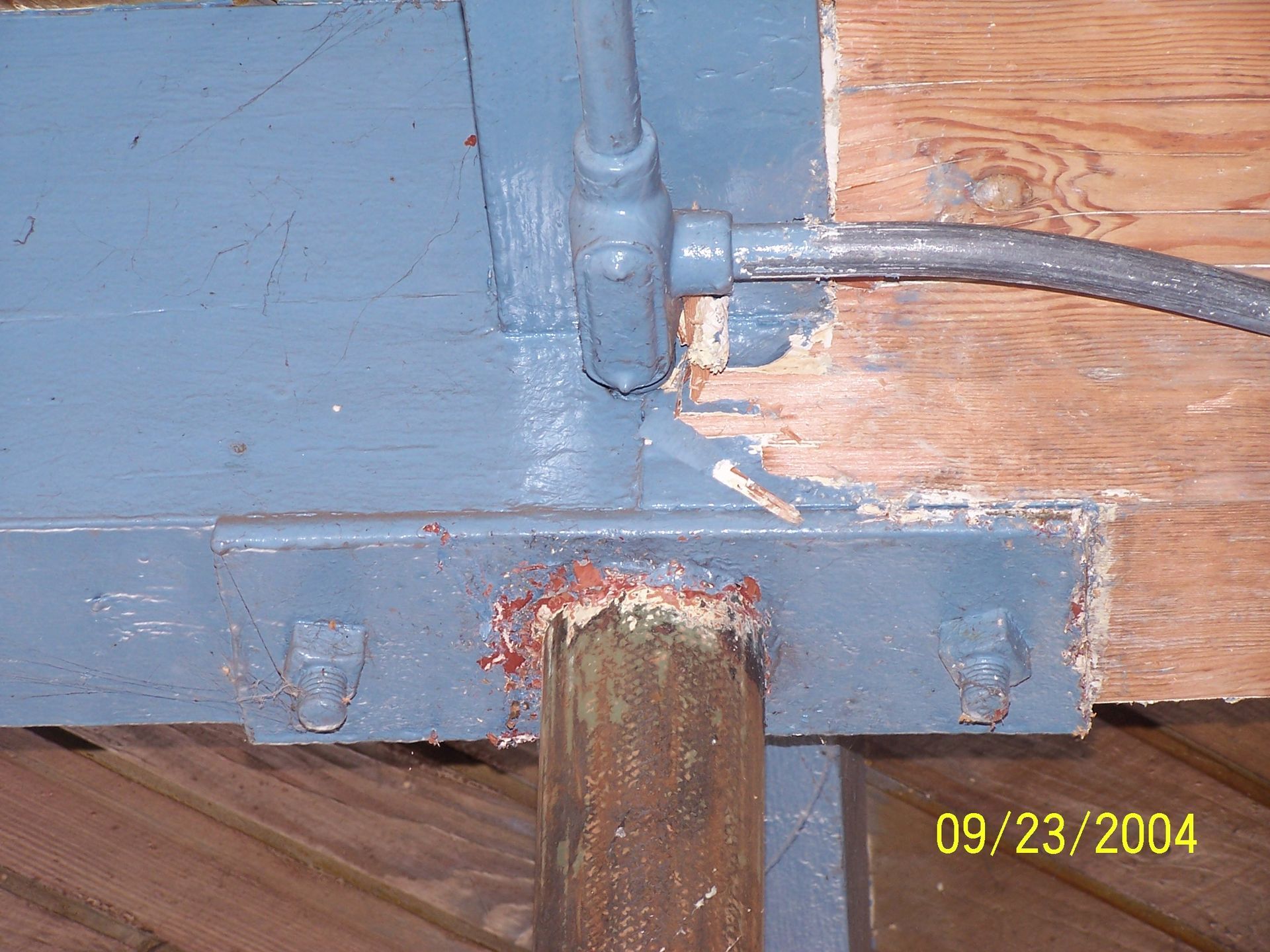Close-up of a blue-painted metal beam with a rusty post and cable attached.