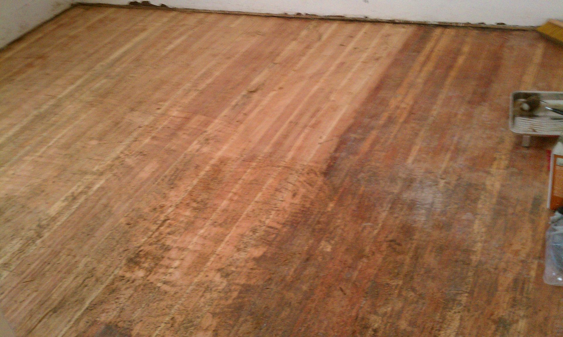 Empty hardwood floor in a room with worn, reddish-brown planks and a white wall
