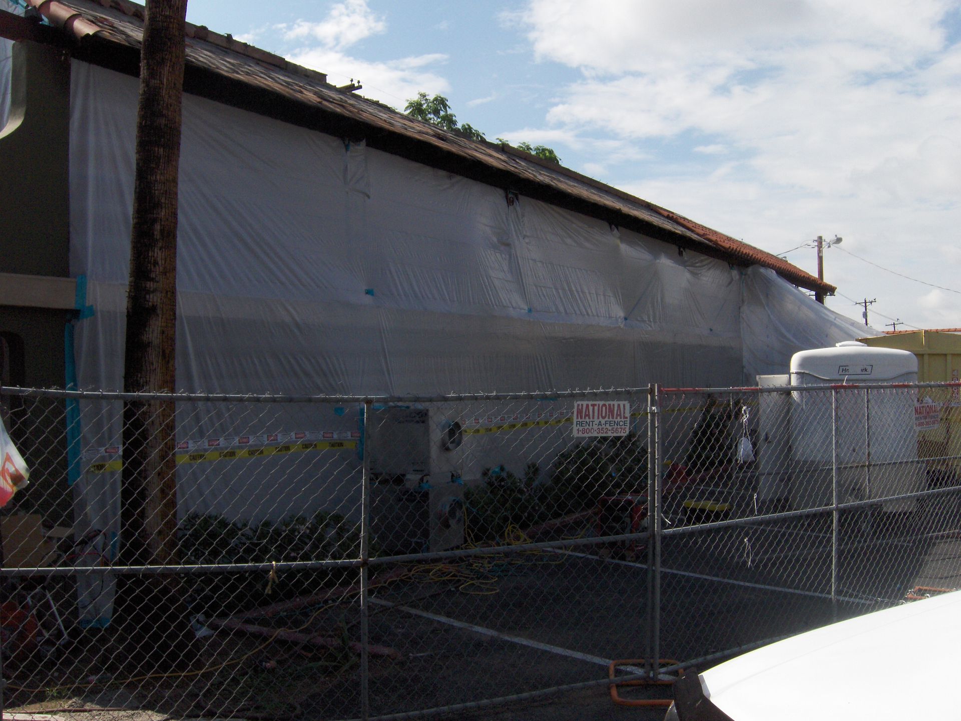 Chain-link fenced industrial building with a gray tarp covering the side under a cloudy sky