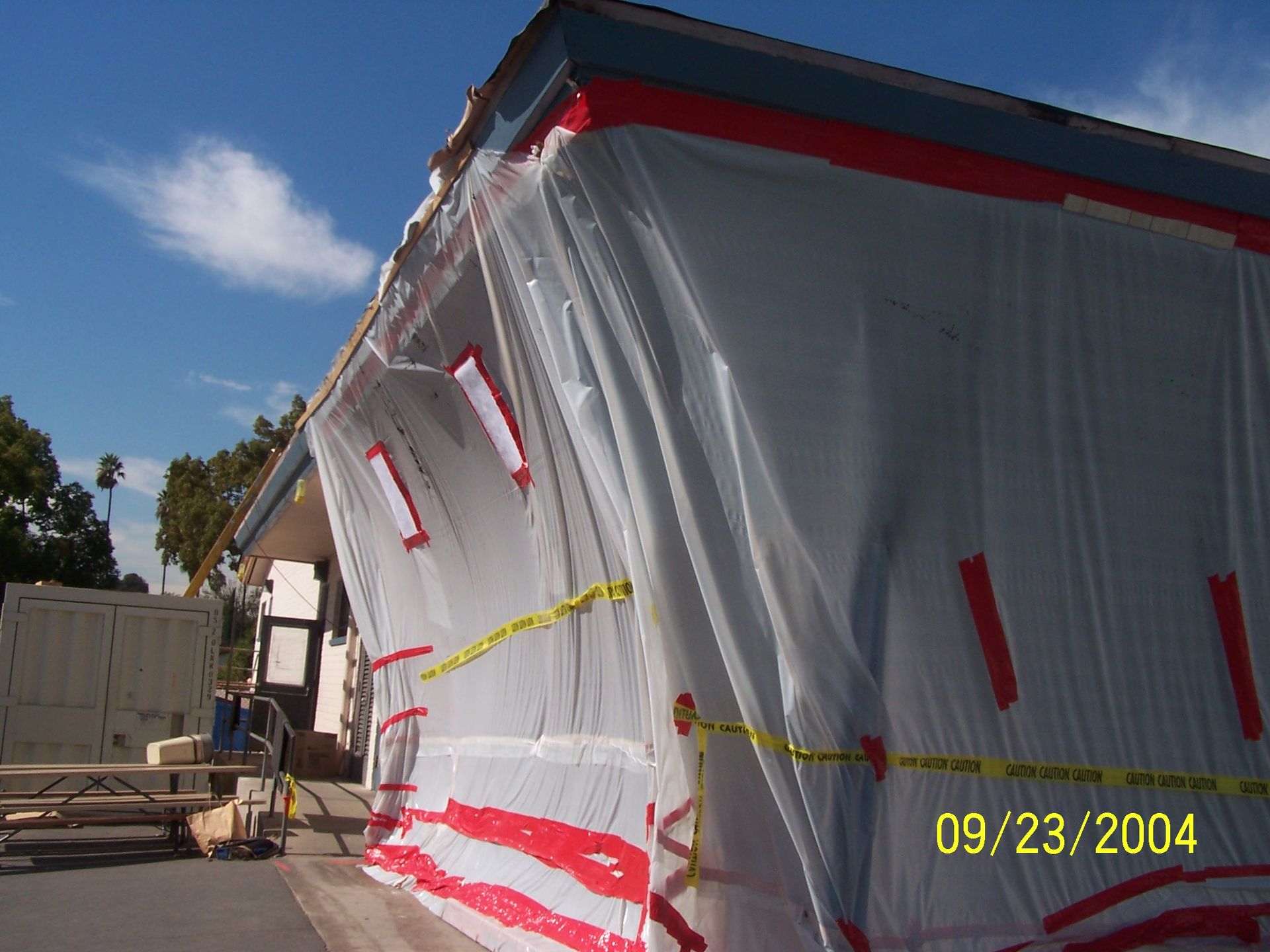 White building wrapped in protective sheeting and red tape at a construction site under a blue sky
