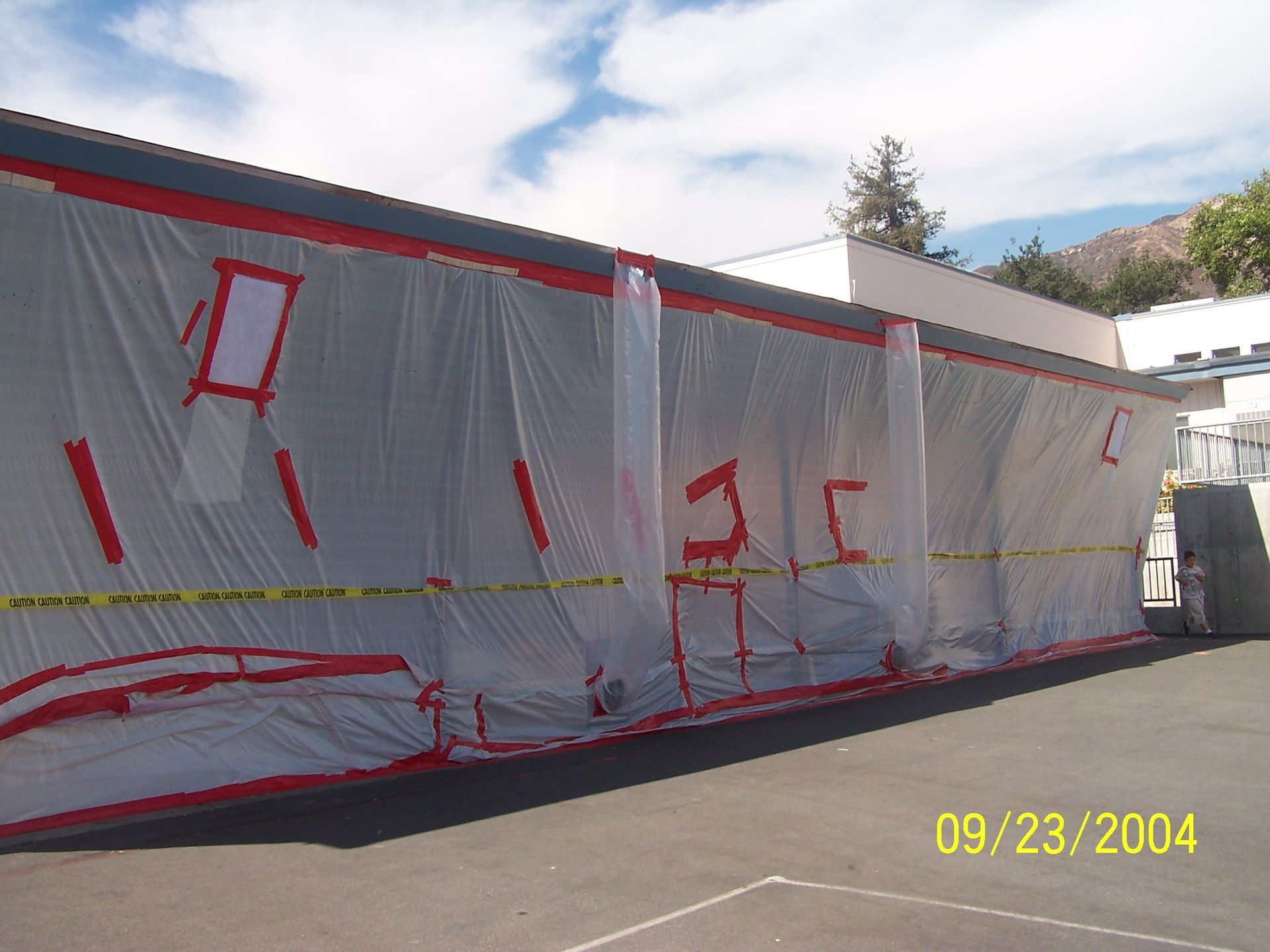 White tarp-covered trailer or structure with red markings on a roadside under a sunny sky.