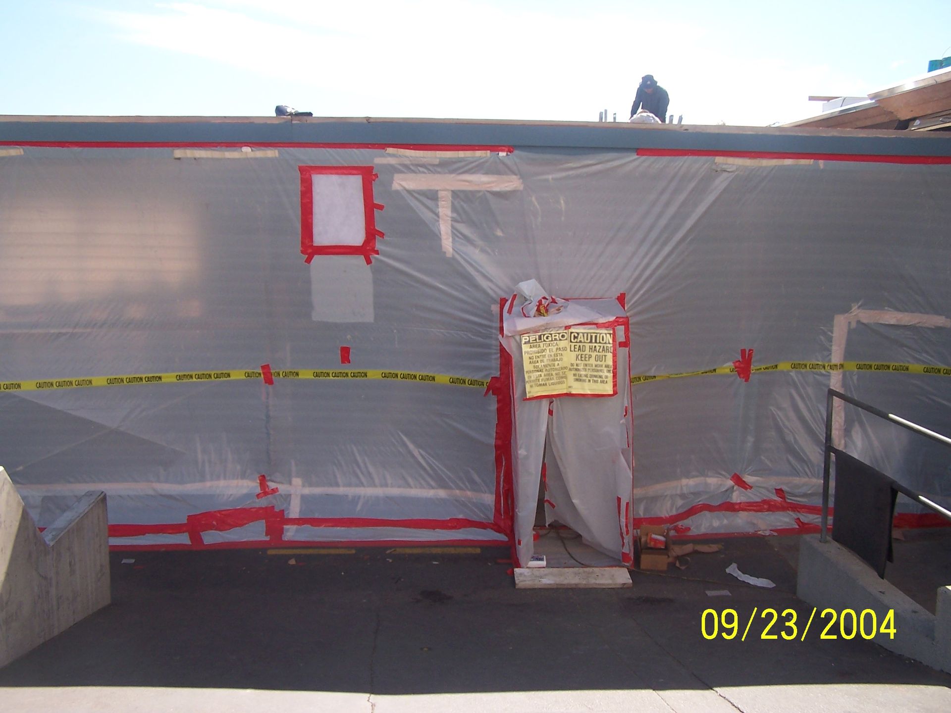 Tarp-covered construction area with taped-off doorway and red-marked windows, date stamped 09/23/2004