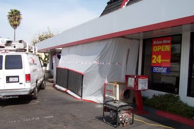 Storefront with a white tarp-covered entrance, taped off sidewalk, and a van parked nearby