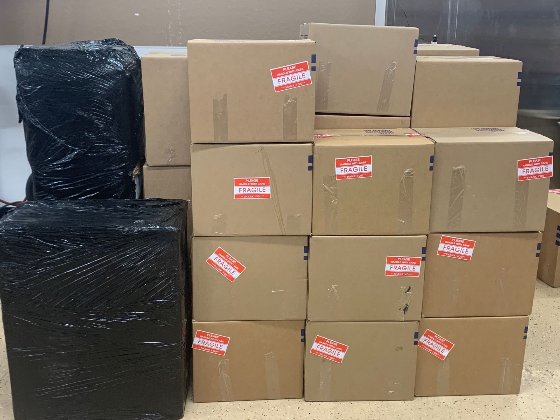 Stacks of cardboard boxes beside two black-wrapped packages in a warehouse or storage area.