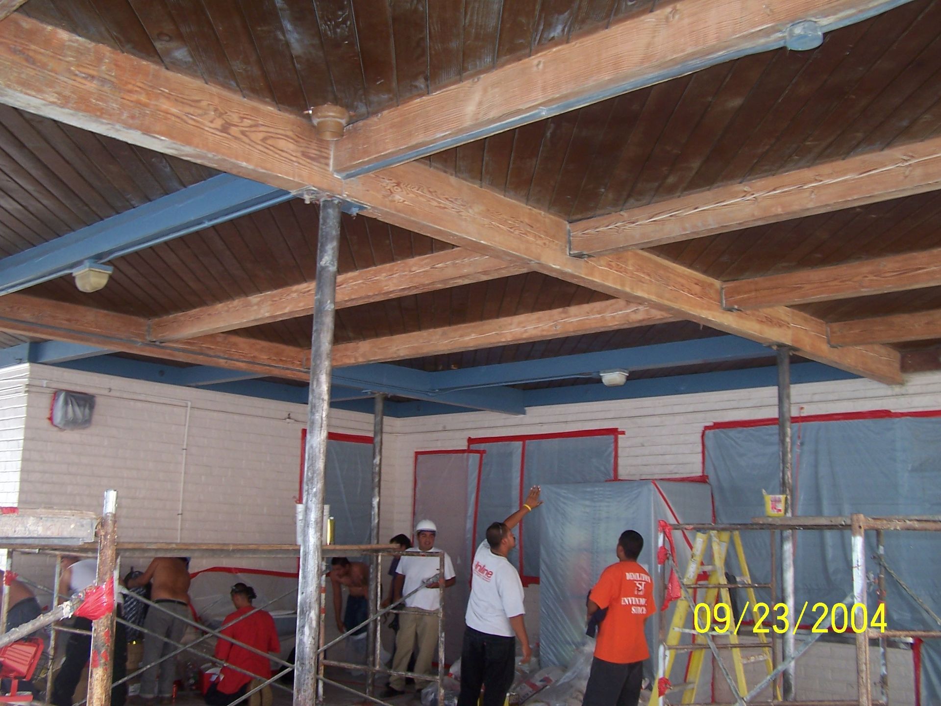 People under a wooden beam ceiling in a room under construction, with scaffolding and tools nearby.