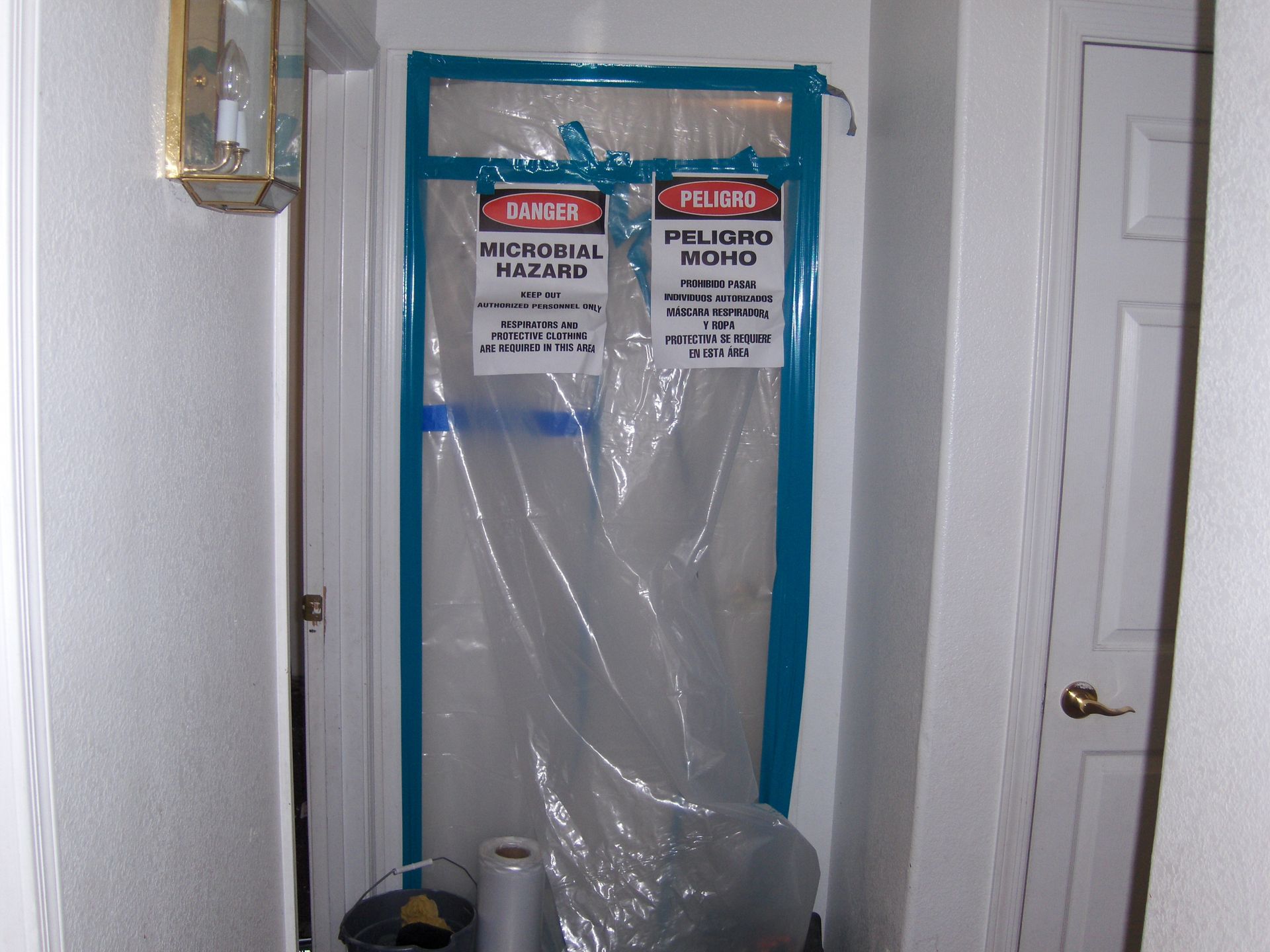 Plastic-covered doorway with blue tape and warning signs in a hallway
