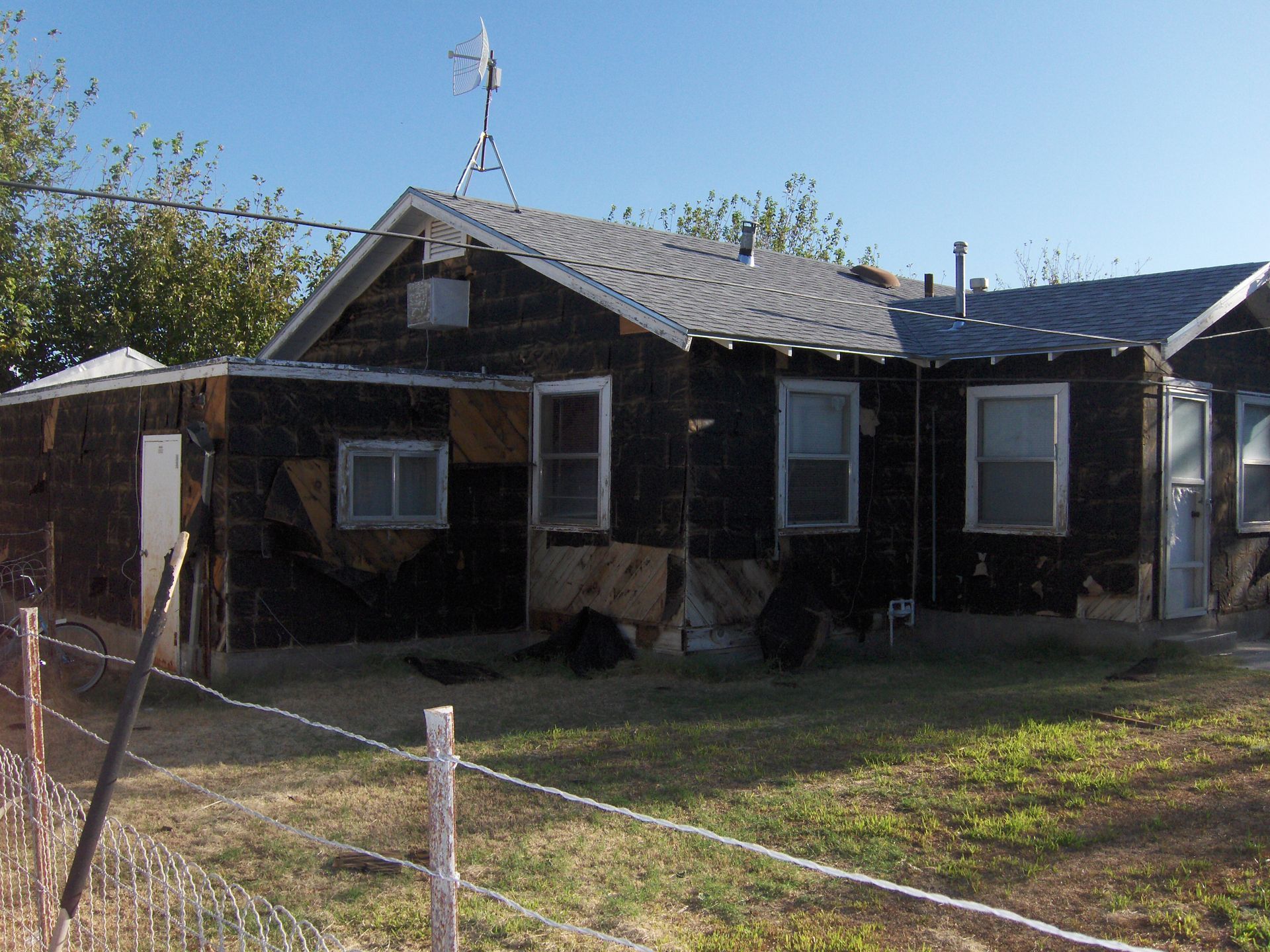 Old weathered house with a fenced yard under a clear blue sky