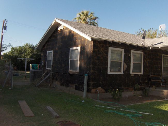 Small dark wooden house with white-trimmed windows and a sloped roof in a grassy yard