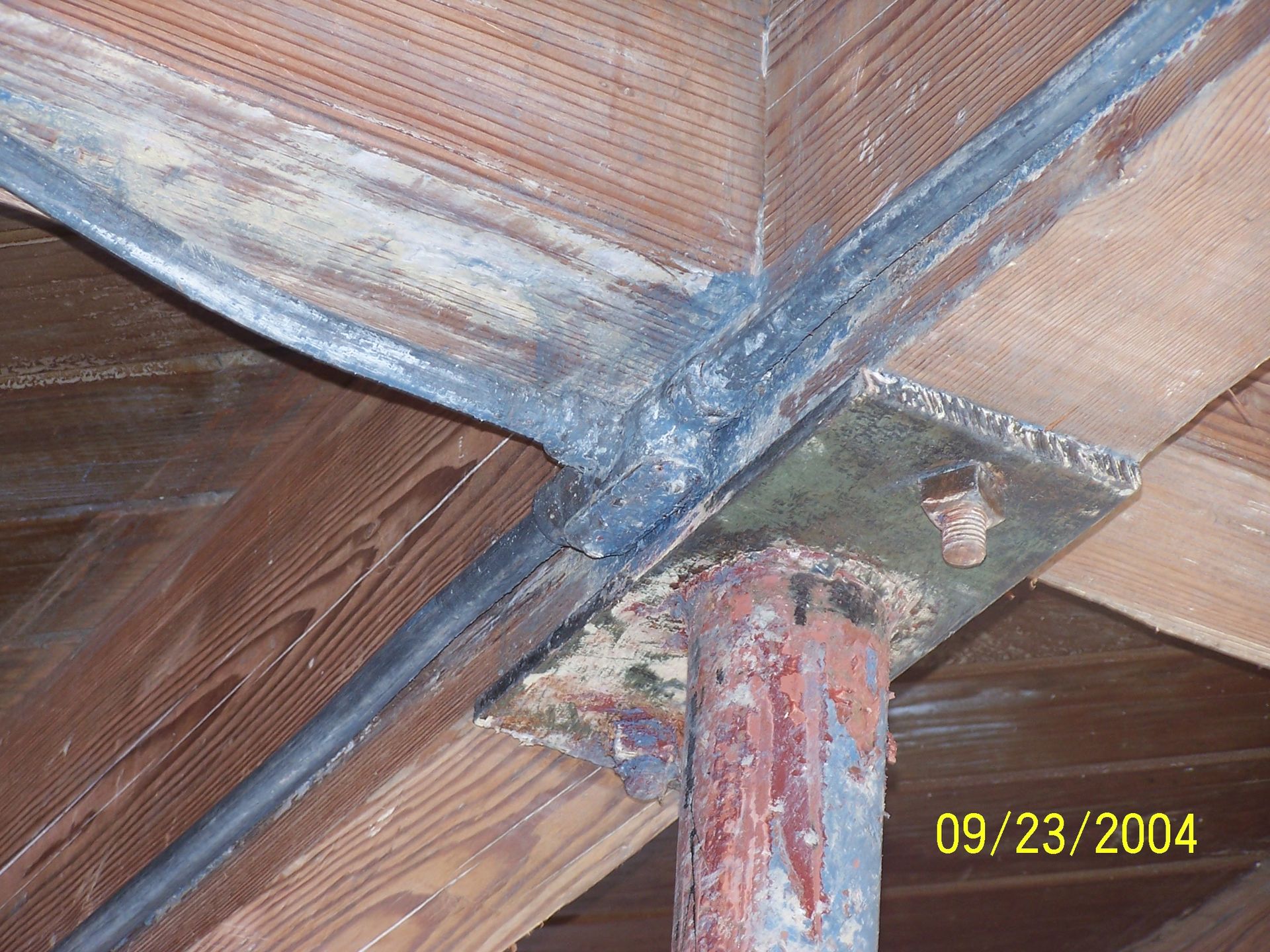 Close-up of a wooden beam joint with rusted metal support and yellow date stamp 09/23/2004