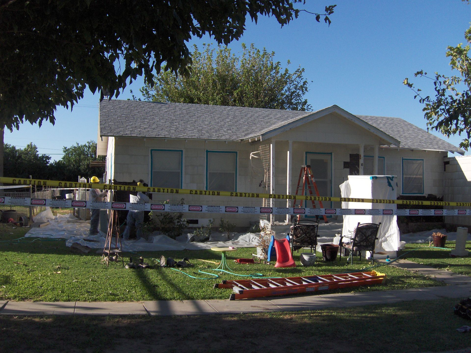 Damaged house under police tape with emergency responders and equipment on the front lawn