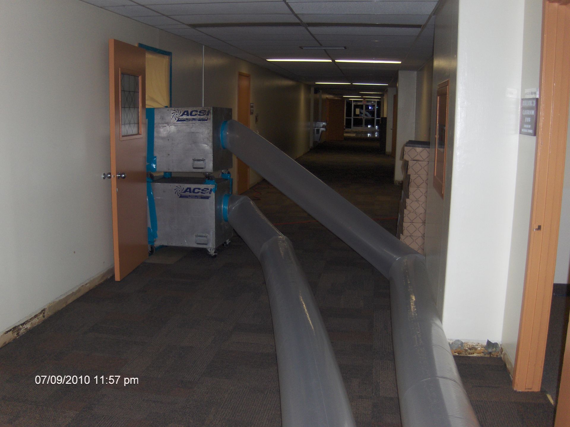Abandoned hallway with two large ducts or pipes running down the floor past stacked boxes.