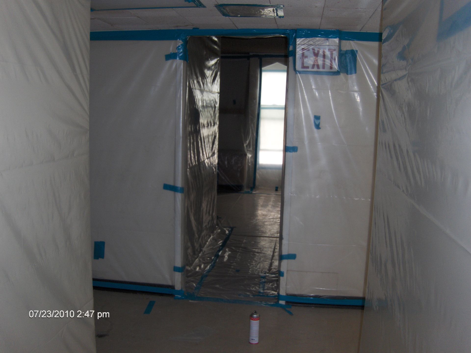Plastic-covered doorway in a narrow hallway, with blue tape and a reflective floor.